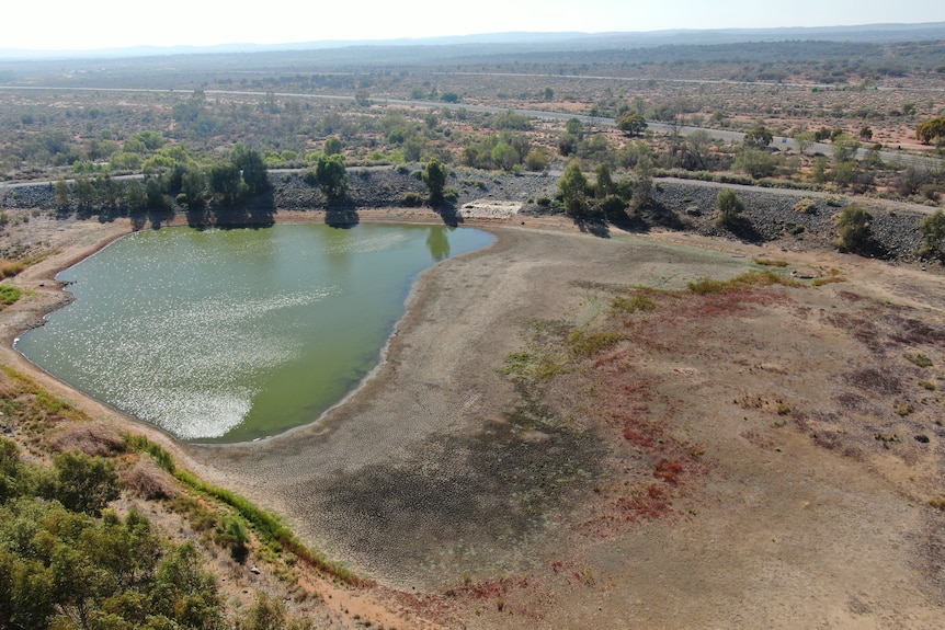 A wide aerial shot of a small body of water which has dried to reveal an expanse of cracked and sparse lakebed