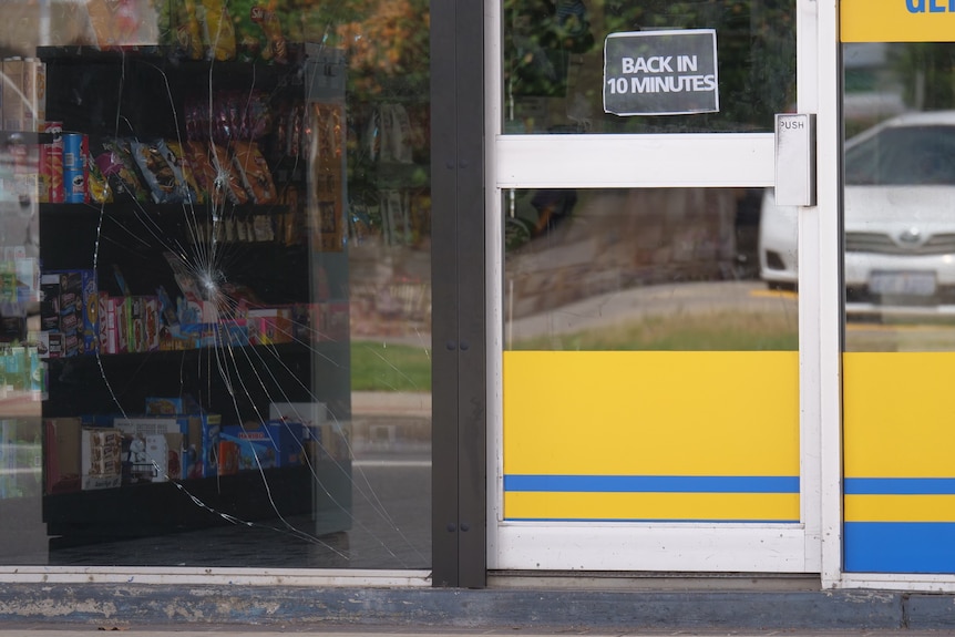 Spider web cracks in Glass next to a door. A sign on the door says "back in 10 minutes".