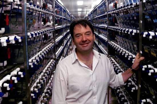 A man in a white shirt standing in an aisle filled with fish tanks