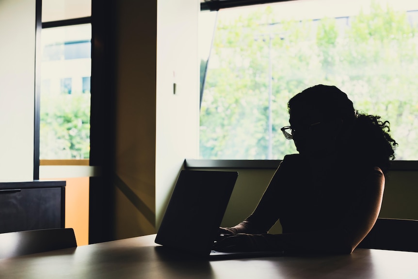 A silhouette of a woman sitting at a table with a laptop.
