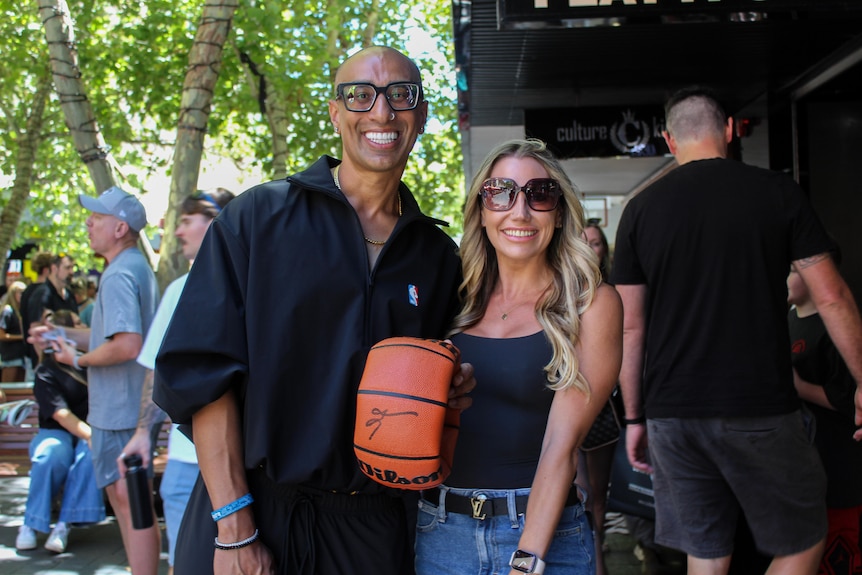 A man and woman stand side by side smiling with a deflated, signed basketball between them