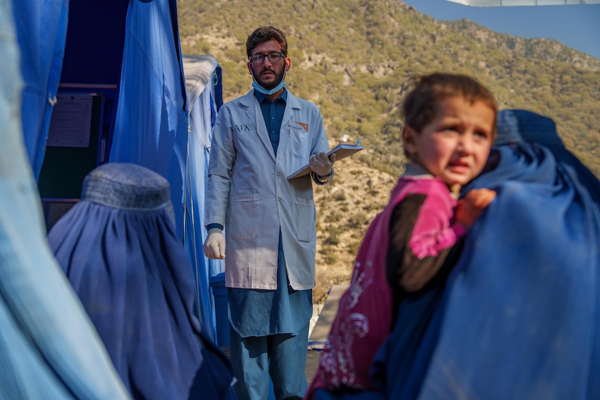 A woman wearing traditional Afghan dress holder her child as she waits in line to see a doctor.