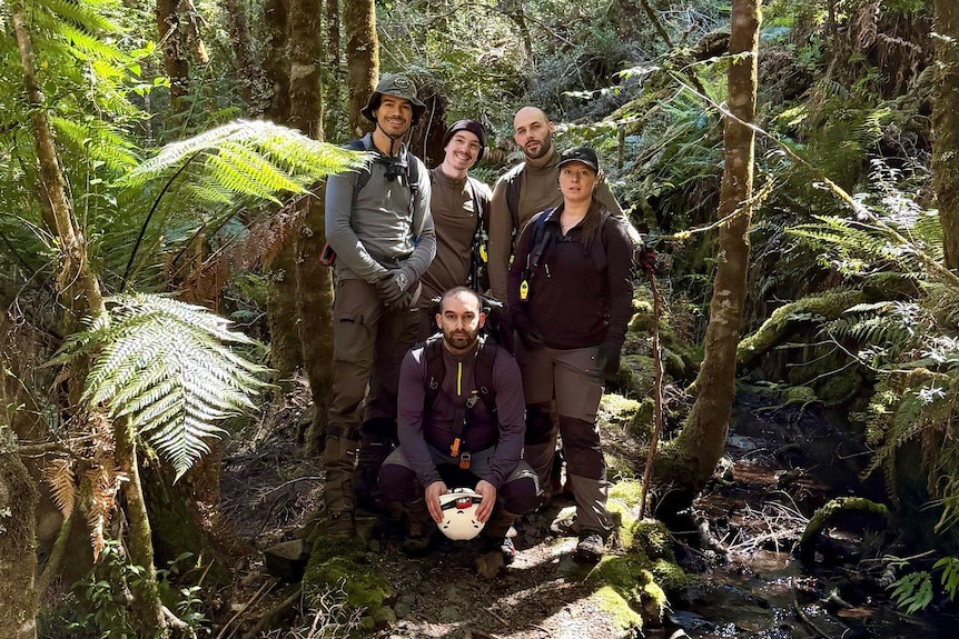 A group of five people standing in thick bushland, smiling at the camera.