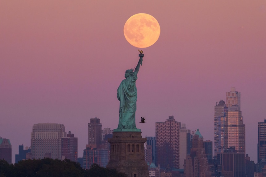 A statue of a woman with a city in the background and a full moon above her head