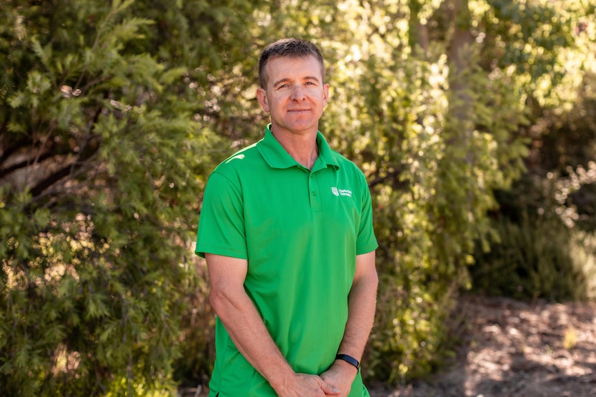 A man in a polo top standing in front of some greenery.