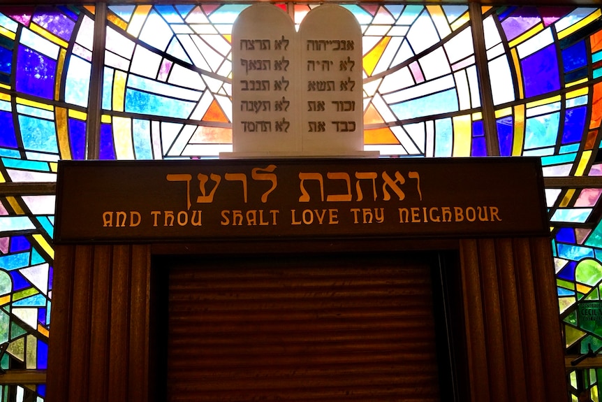 Inside Emanuel Synagogue with a sign that reads And Thou Shalt Love Thy Neighbour, in front of stain glass.