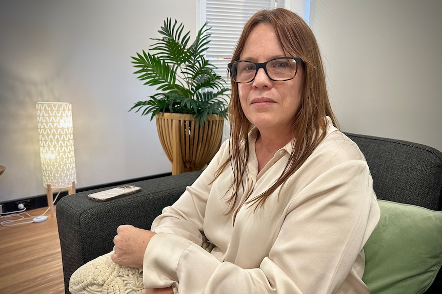A woman sits on a couch looking at the camera