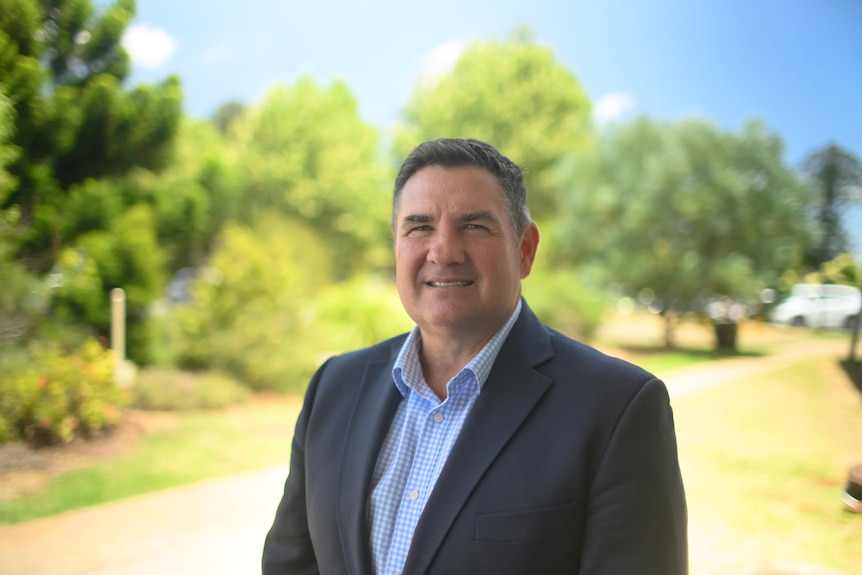 A man in a suit against a leafy backdrop