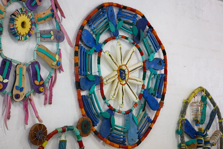 Thongs and pieces of coloured plastic hang on a white wall as pieces of artworks.