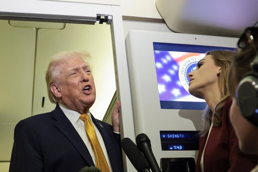 Donald Trump speaking to a reporter in the aisle of an airplane cabin.