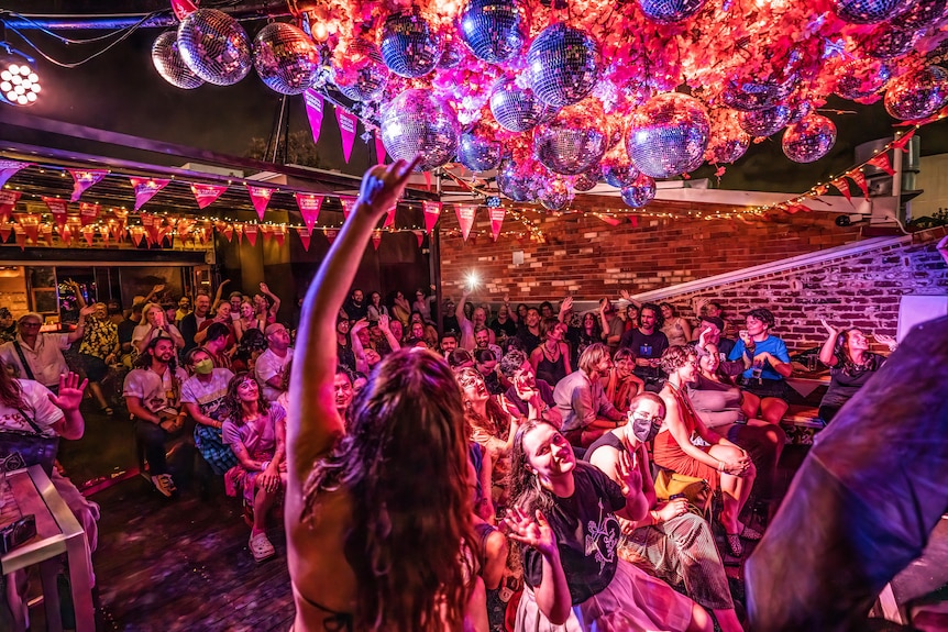 A performer is pictured from the back in front of a packed venue sitting beneath disco balls