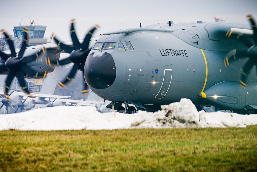 A Luftwaffe plane with propellors in action taxis over snowy ground.