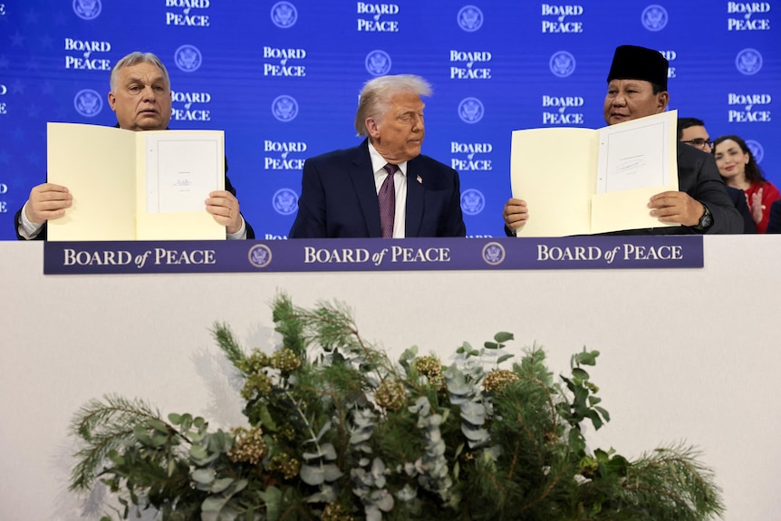 Two men showing a signed documents with one man looking to his left in the middle.