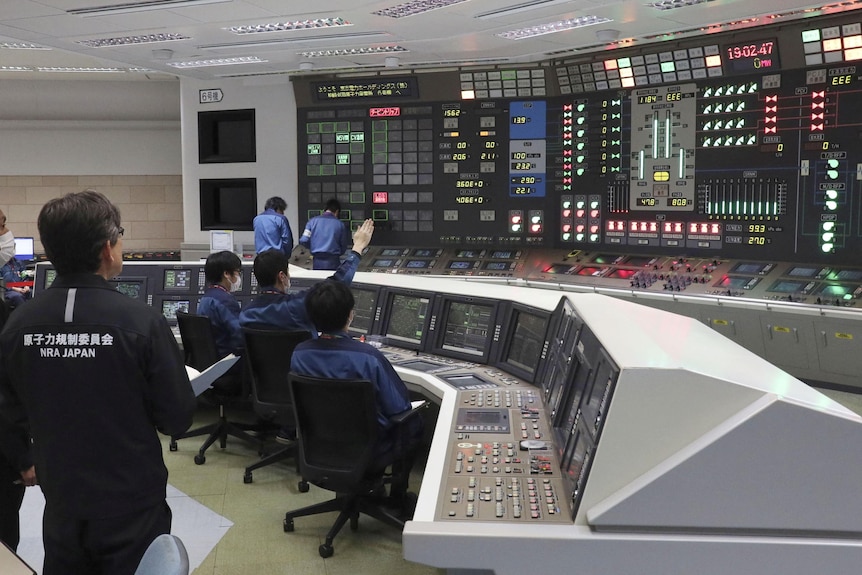 People in blue uniforms sit behind a large desk looking at digital screens