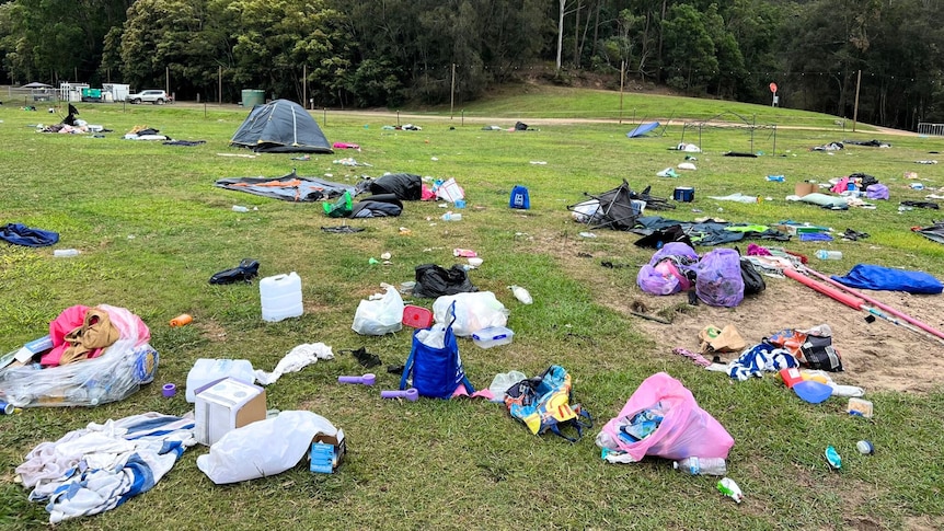 scattered bags of trash, camp chairs, tents and misc camping gear on a grassy field