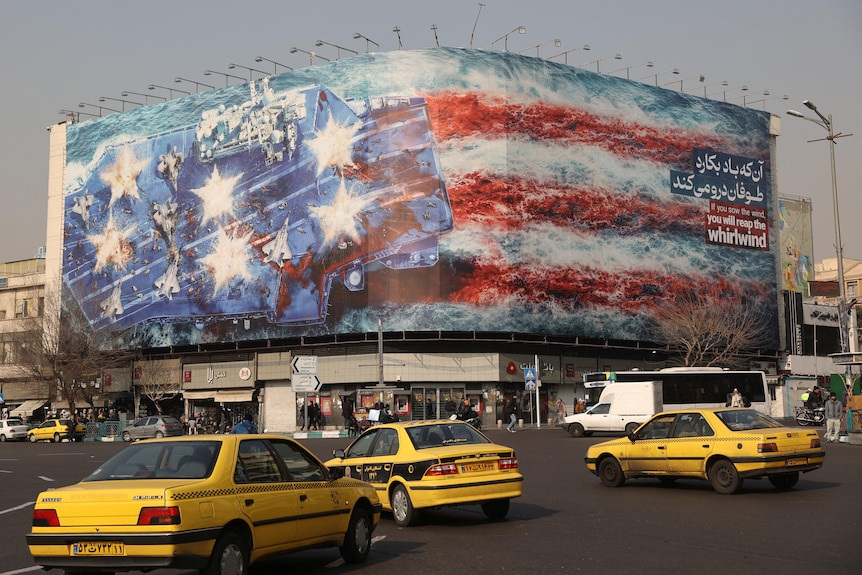 A large billboard on a street corner showing a US aircraft carrier being bombed.