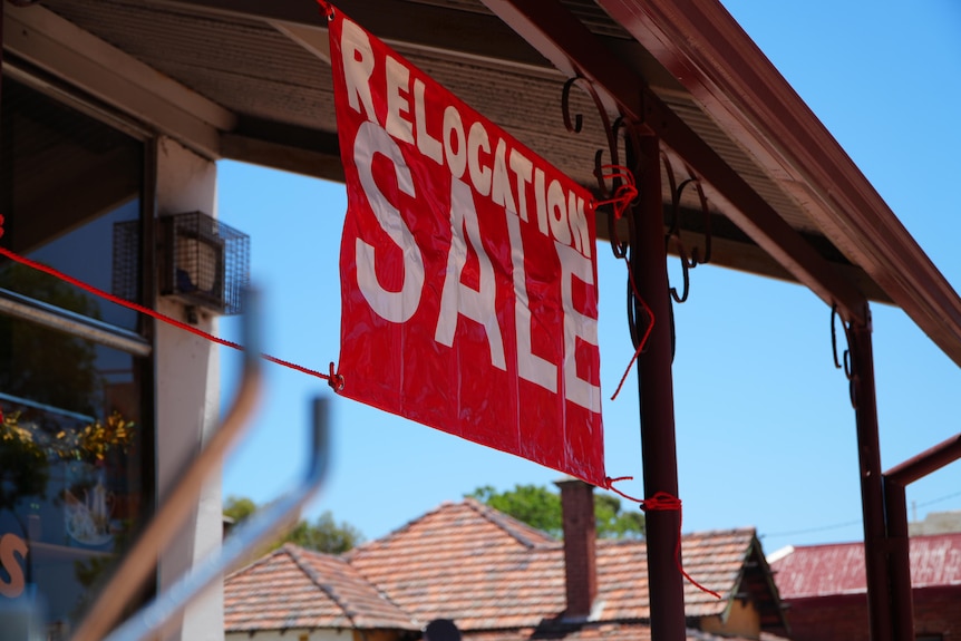 A red 'relocation sale' sign hangs under an awning outside a shop.