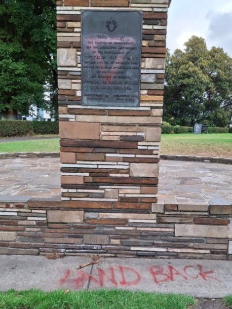 A rectangular brick monument is spray-painted with the words 'Land Back' in red paint.