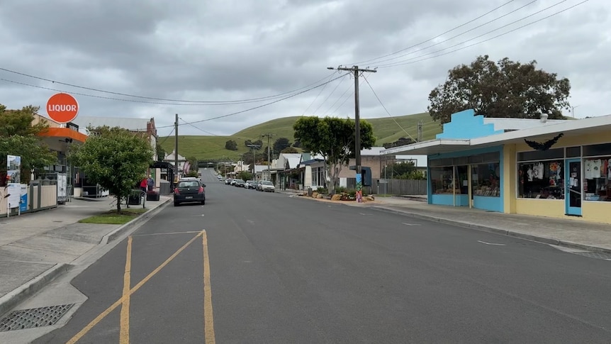 A photo of peaceful street of a country town, with green hills in the background and a cloudy sky