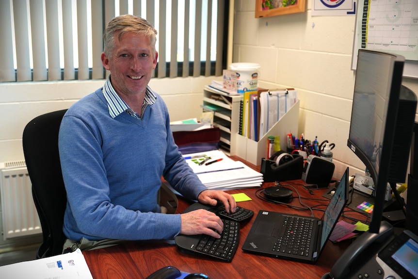 Ed, a man wearing a blue jumper and striped shirt, sits at a computer.