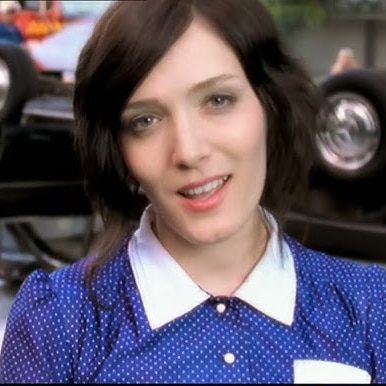 Person in a blue polka-dot shirt stands in front of an overturned car and emergency crew.
