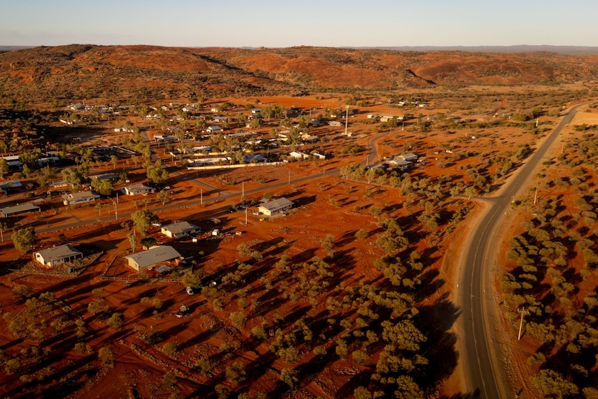 A drone shot of the houses in Mimili, a road leading to it can be seen and a rocky mountain behind the community. 