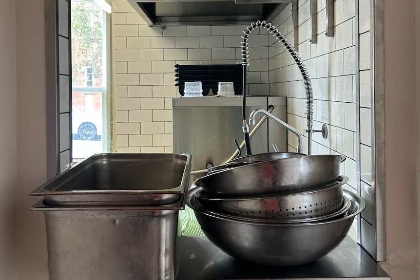 Stainless steel tins and bowls stacked on a kitchen bench.