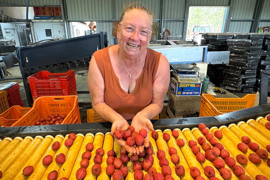 Annette holds up lychees behind a conveyor belt full of fruit.
