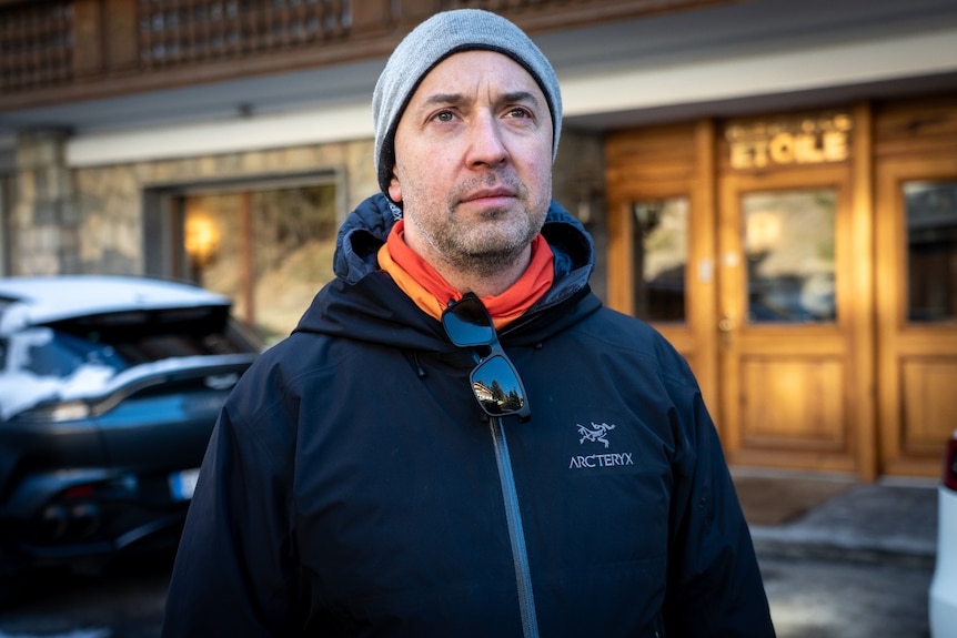 A man with cold-weather clothes on looks on with a neutral expression on his face.