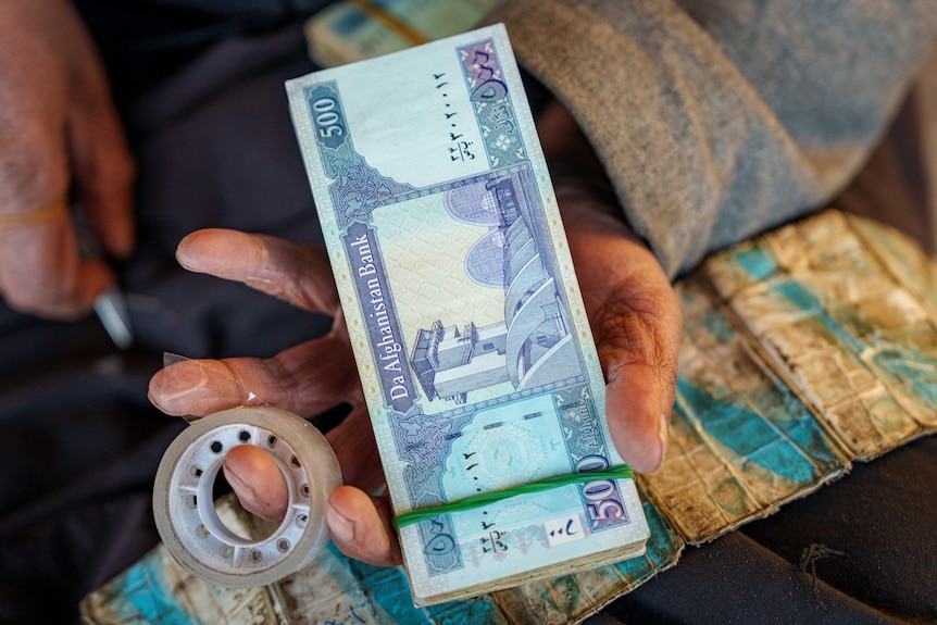 A man holds up a stack of Afghan cash.