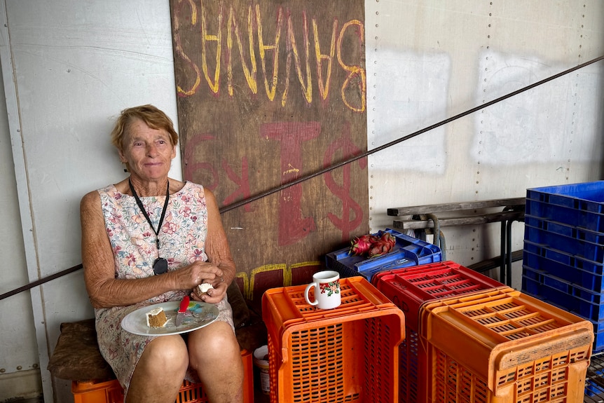 A woman eats cake, sitting on a crate.