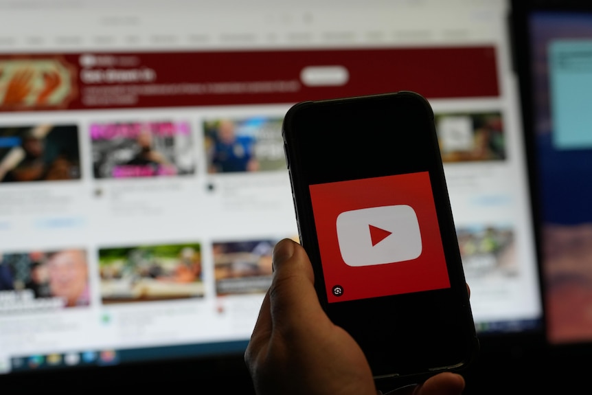 A smartphone with the YouTube logo, with the website in the background behind it.