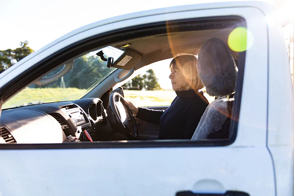 A senior female driver sits behind the wheel of a ute. 