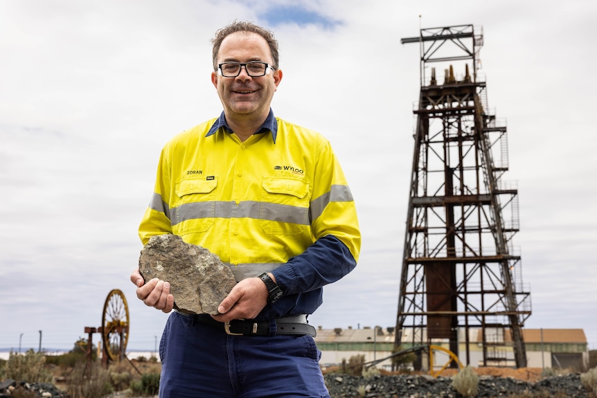 A mining executive holding nickel ore with a mine headframe in the background.  