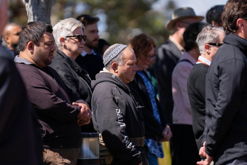 A crowd of solemn-looking people standing outdoors.