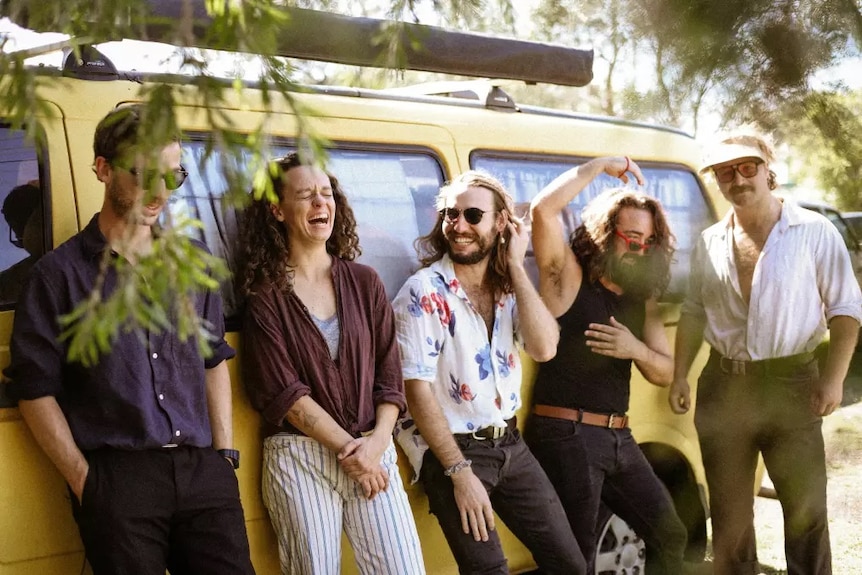 Bluegrass band Midnight Chicken lean together on a van laughing.