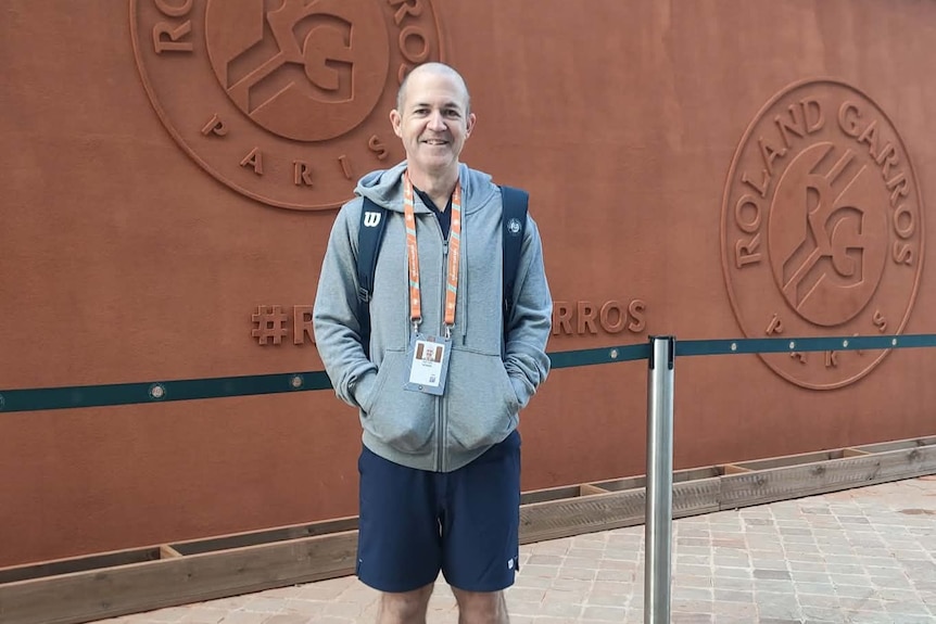 Man wearing jumper smiling stands in front of Roland-Garros wall