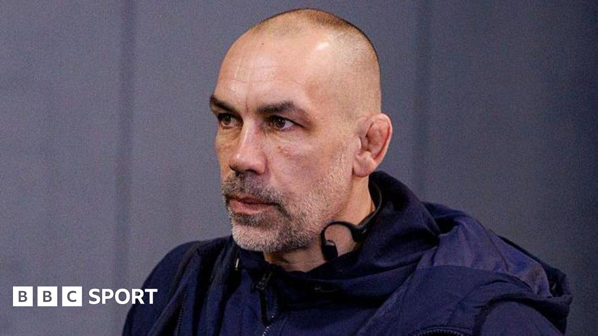 Alex Sanderson looking straight ahead with a grey wall behind him