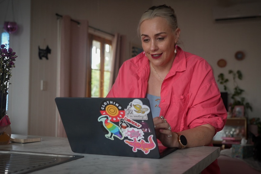 A photo of author Melanie Saward writing at her laptop with a pink shirt on.