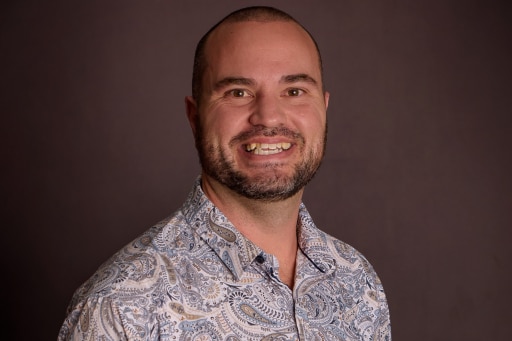 A man with a beard smiles with a dark background.