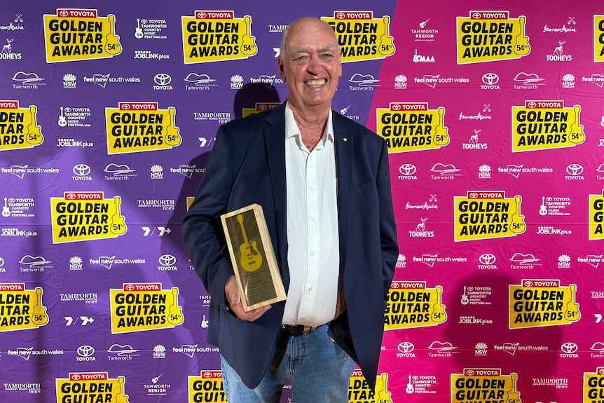 A man in a suit smiles holden a award