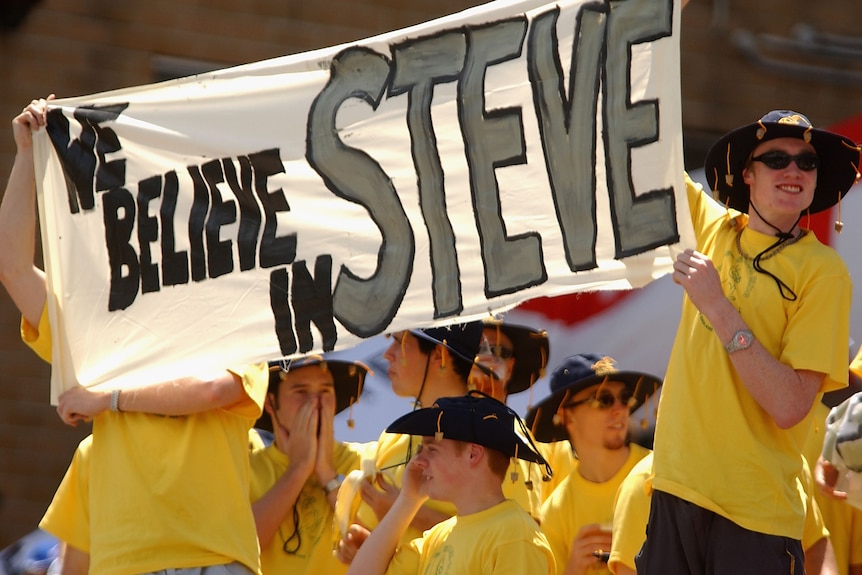 A group of cricket fans hold up a banner that reads "we believe in Steve"