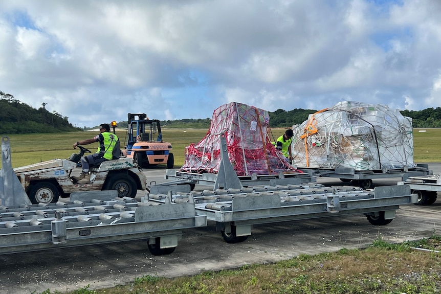 A trailer loaded up with polystyrene boxes being pulled by a small tractor at an airport.