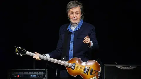 Getty Images Sir Paul Mccartney stands on stage with a guitar and pointing towards the crowd