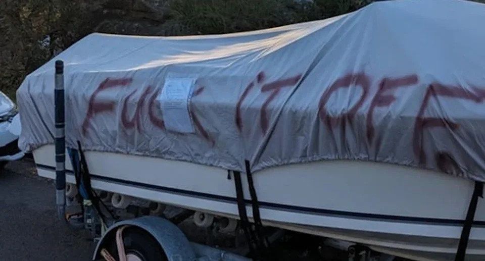 A boat with a tarp covering it and the words 'fuck it off' spray painted on it. 