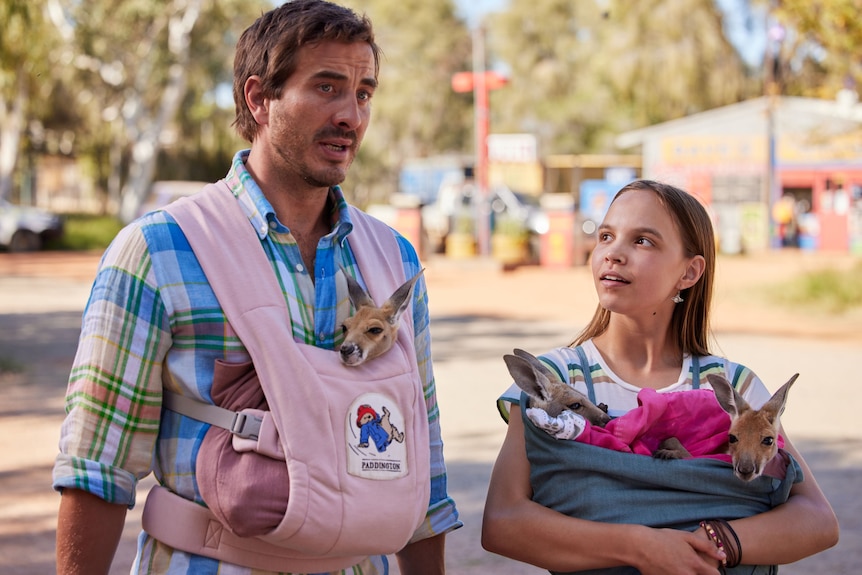 A film still of Ryan Corr, 37, and Lily Whiteley, a 15yo Indigenous girl, each with a joey or two in a carrier or their arms.