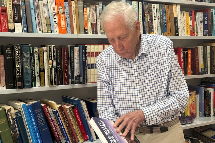 Professor Peter Cook reads a book in front of a large, well stocked book shelf.
