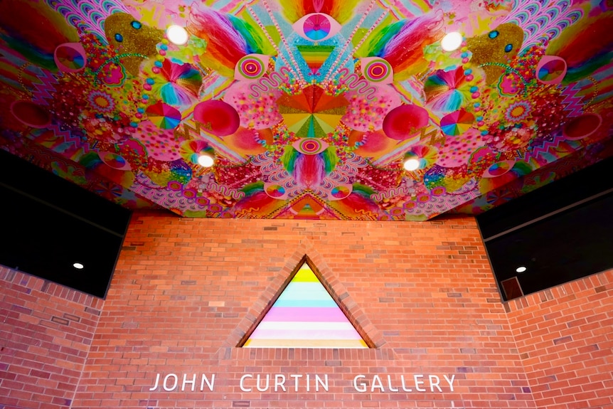 A wide shot of a ceiling and wall with a sign reading: John Curtin Gallery 