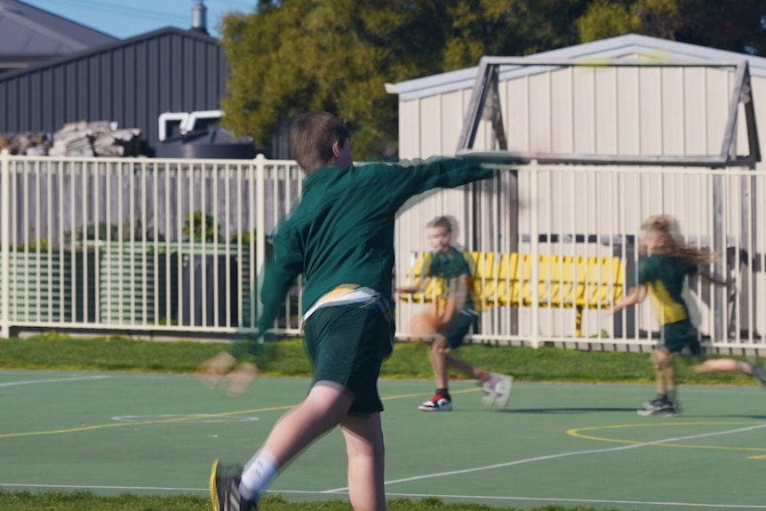 A student wearing a green jumper throws a ball across a green pitch.