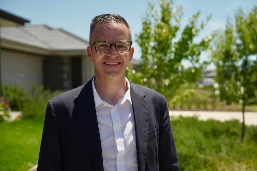 Stefan Koormen standing in front of a blurred house with green front yard grass and trees.